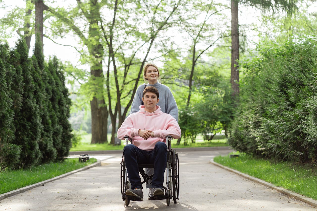 A couple enjoying a sunny day in the park, one in a wheelchair, pushing forward with a smile.